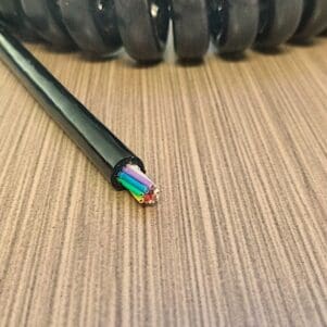 A EC2812 - Electronic Coiled Cord 28 Gauge with 12 Conductors - No Shield wire is sitting on top of a wooden table.