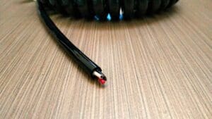 A black and red EC203 - Electronic Coiled Cord 20 Gauge with 3 Conductors - No Shield on a wooden table.