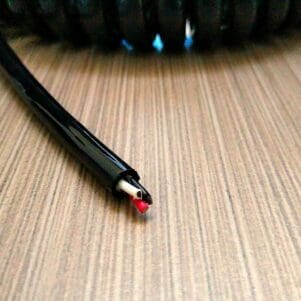 A black and red EC203 - Electronic Coiled Cord 20 Gauge with 3 Conductors - No Shield on a wooden table.