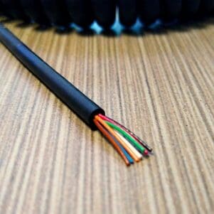 An EC307 - Electronic Coiled Cord 30 Gauge with 7 Conductors - Non Shielded wire is sitting on top of a wooden table.