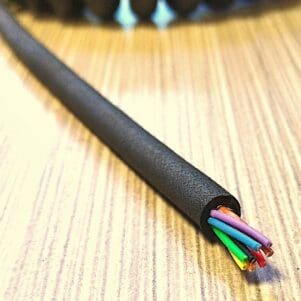 A PCO129 - Power Coiled Cord 12 Gauge with 9 Conductors - No Shield - 600 Volts cable laying on top of a wooden table.