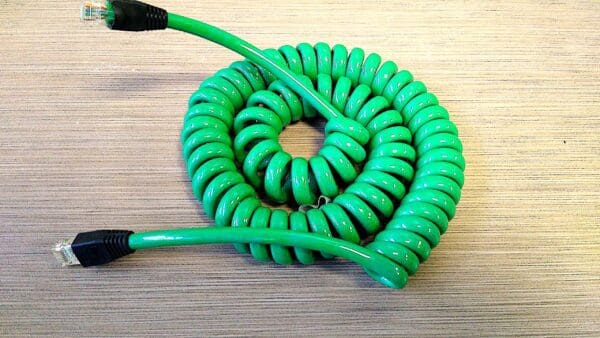 A 3 Ft. Length - NCC4PR24A SCI-FLEX COILED CAT5e 4 ETHERNET 24GA PAIRS W/ RJ45 PLUGS - ONLINE DEAL! Use Code CS23 - Electric Lime Green coiled cord on a table.