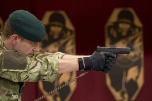 A soldier is holding a Tactical Pistol Lanyard - NON-ELECTRIC COIL CORDS - NEC100 in front of a wall.