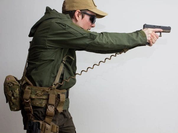 A man holding a Tactical Pistol Lanyard - NON-ELECTRIC COIL CORDS - NEC100 and aiming at a white wall.