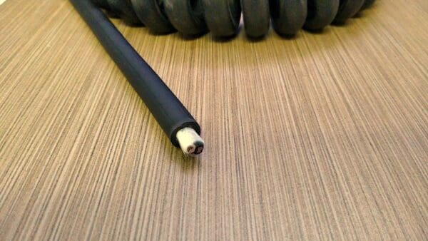 A black PCE142 - Power Coiled Cord 14 Gauge with 2 Conductors - No Shield on top of a wooden table.