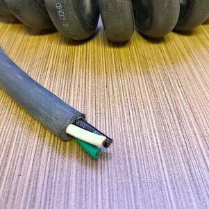 A PCO143 - Power Coiled Cord 14 Gauge with 3 Conductors - No Shield - 600 Volts cable on a wooden table.