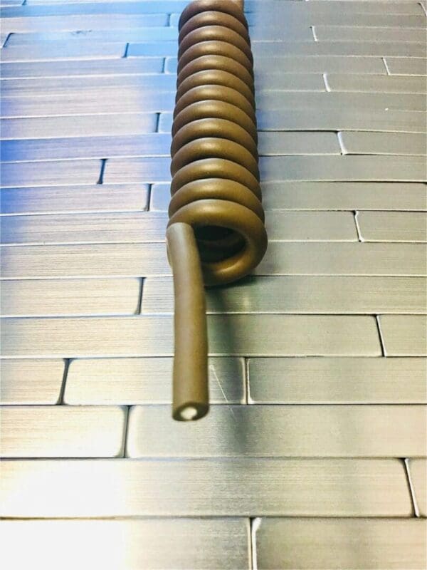 A Tactical Pistol Lanyard - NON-ELECTRIC COIL CORDS - NEC100 on a metal surface.