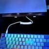 Colorful backlit mechanical keyboard with a USB 3.2 Male-A to Male-C Coil Cord - SS 10GBPS connected to a closed laptop in the background, on a dark desk.
