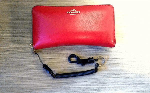 Red coach wallet with a High Performance Coiled Lanyard Safety Tether attached, lying on a wooden surface.