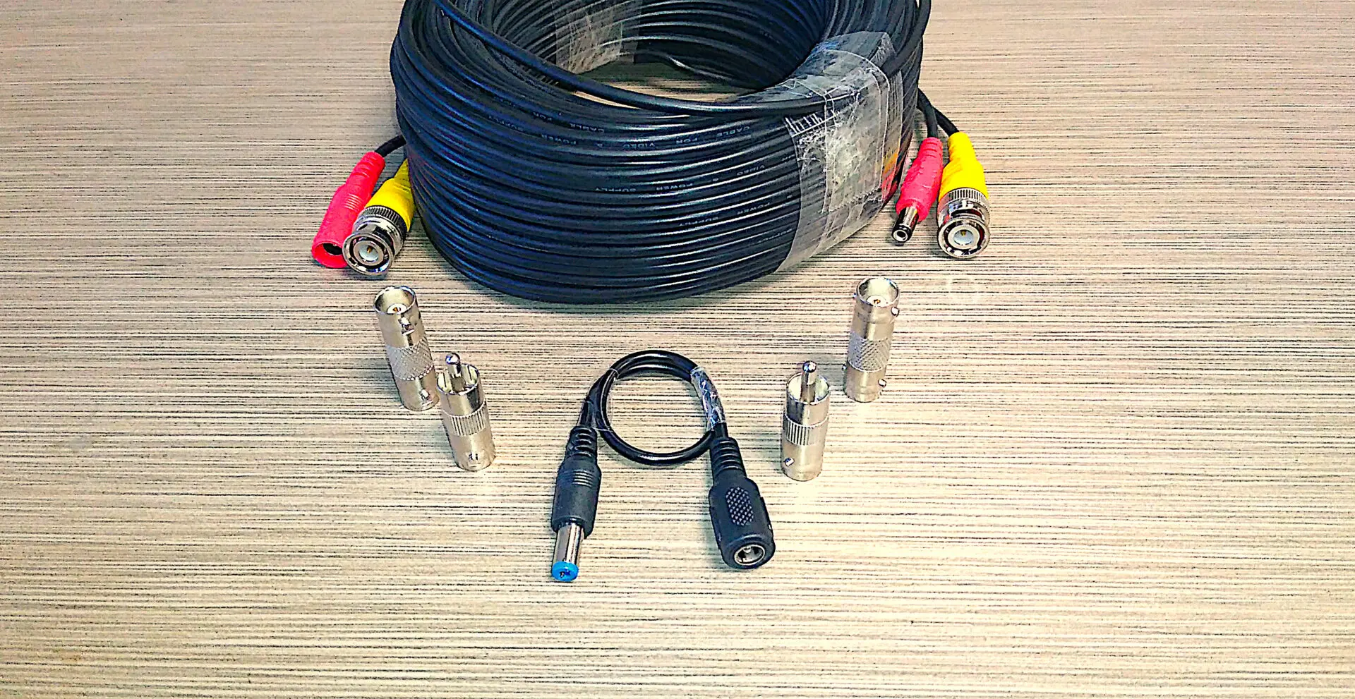 A collection of Video Security Camera Wire with Connectors for CCTV Camera DVR Surveillance System, including a coiled black cable and various types of metal plugs, arranged on a textured surface.