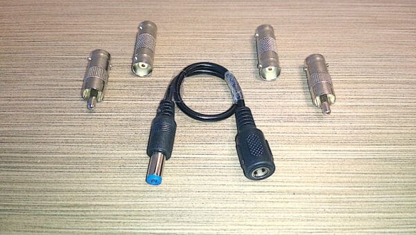 Assortment of electronic connectors including four BNC connectors and a Video Security Camera Wire with Connectors for CCTV Camera DVR Surveillance System on a wooden surface.